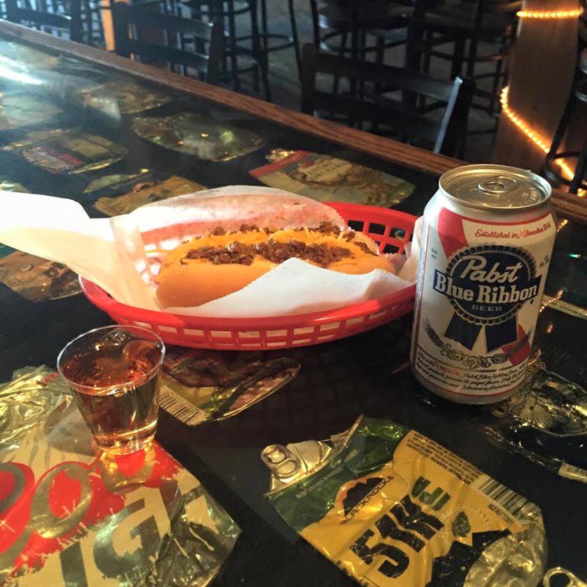 A grilled cheese in a red basket with a PBR can on the bar top.